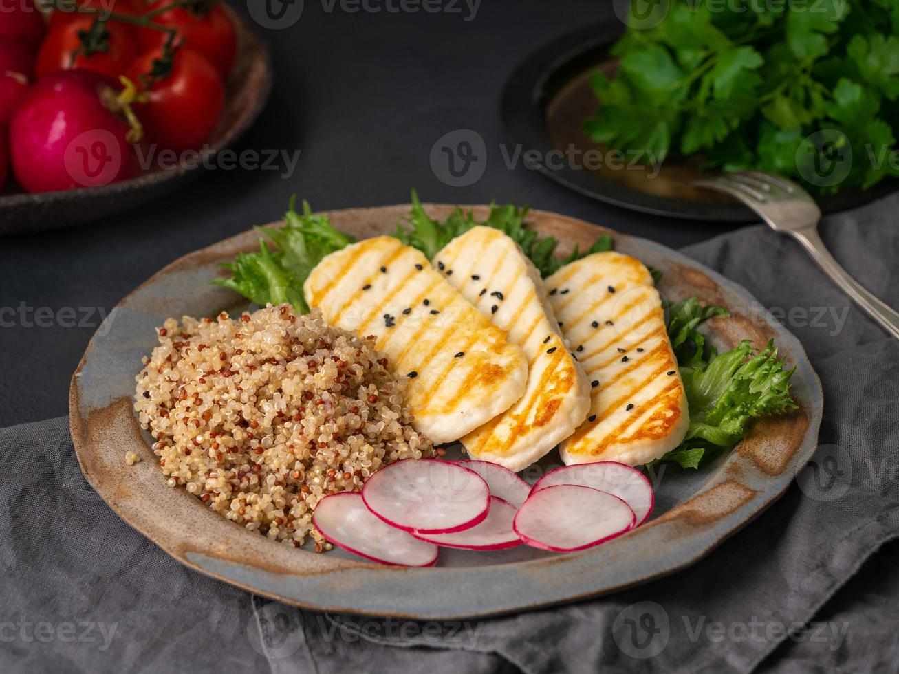 halloumi, queso a la parrilla con quinua, ensalada, rábano. dieta equilibrada sobre fondo oscuro, vista lateral foto