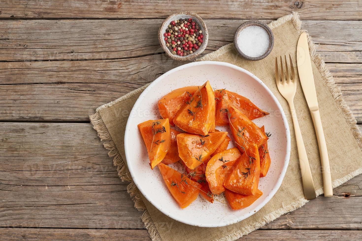 calabaza asada, piezas en plato con miel y condimentos, antigua mesa rústica de madera oscura foto