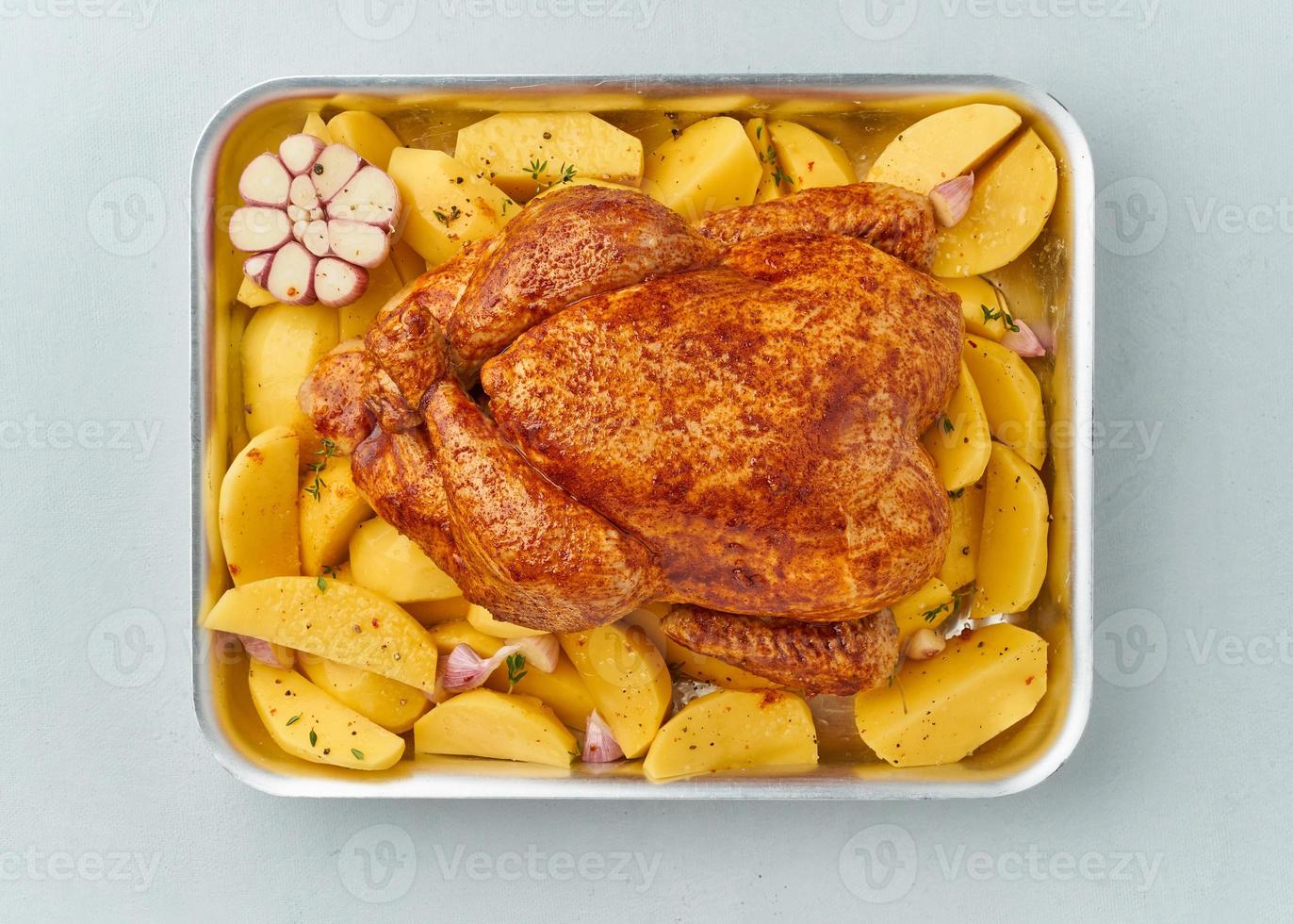 whole marinated chicken in sauce with raw potatoes in baking dish photo