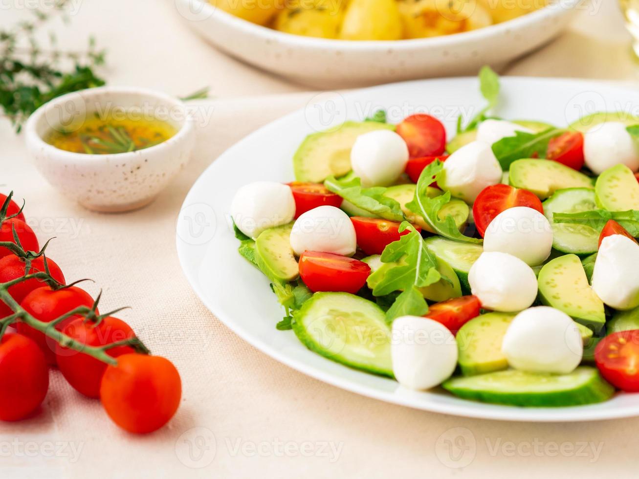 Fresh salad with tomatoes cucumbers arugula mozzarella and avocado. Oil with spices rosemary thyme, side view photo