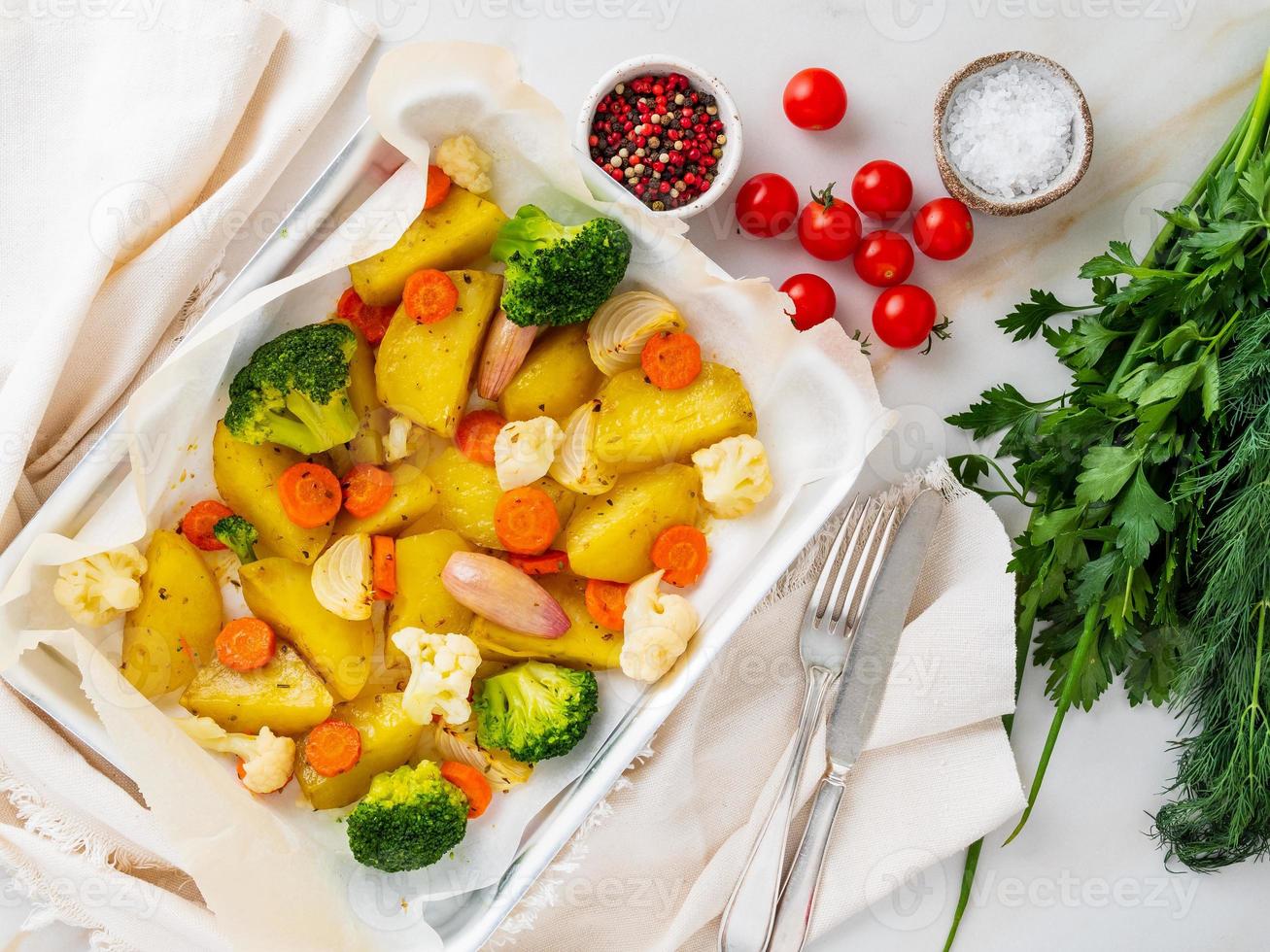 Roasted vegetables on tray with parchment on marble table. Potatoes, carrots, photo