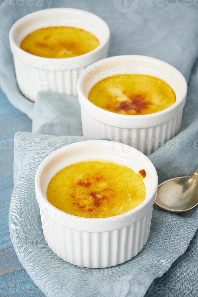 crema catalana, postre español en tres ramekin sobre mesa azul, vertical foto