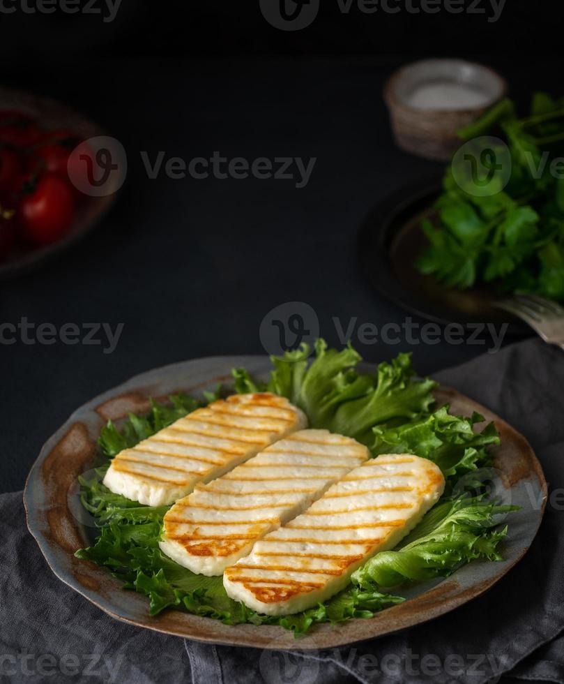 halloumi a la parrilla, queso frito con ensalada de lechuga. dieta equilibrada sobre fondo oscuro, vista lateral, vertical foto