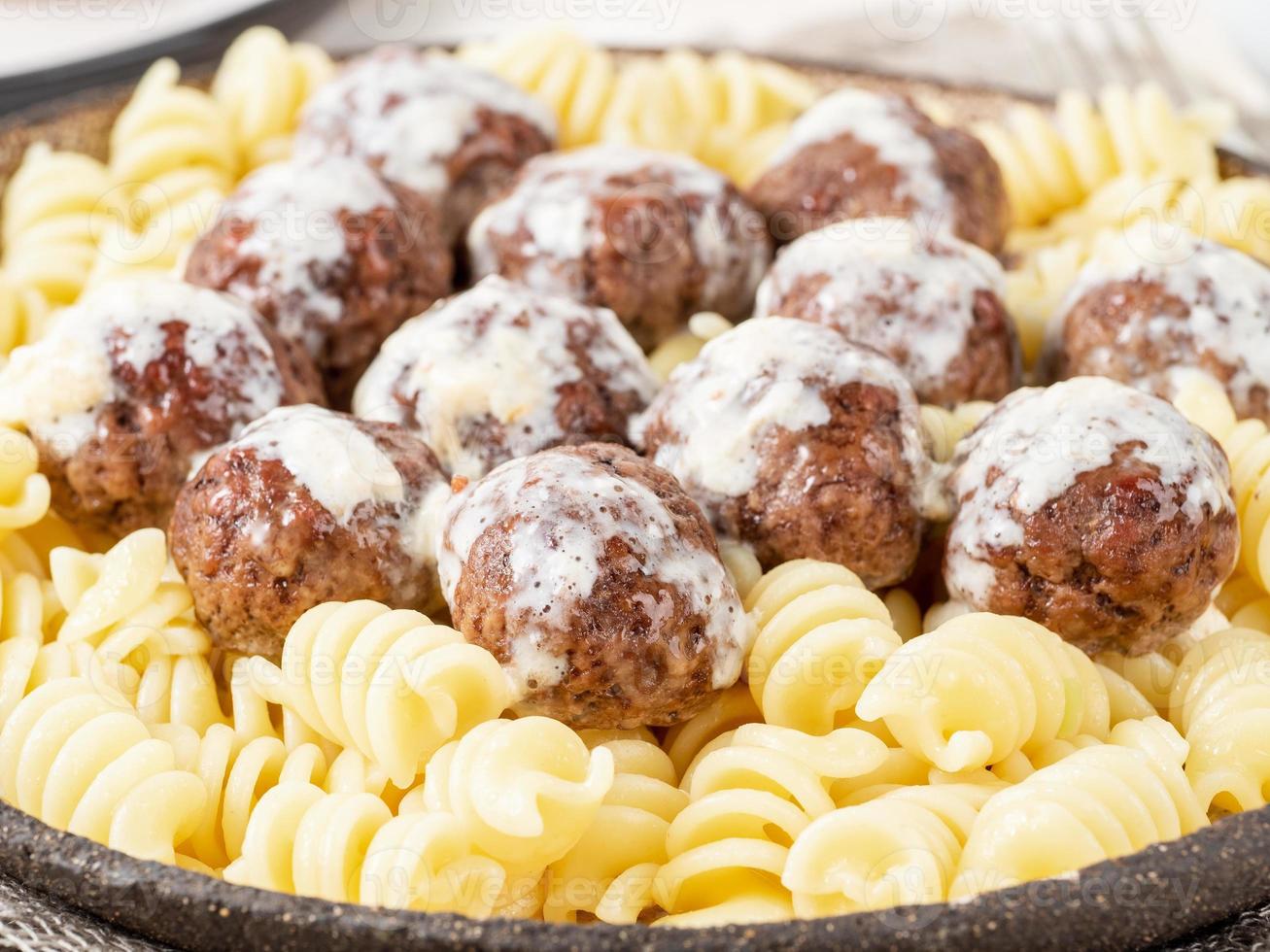 Swedish meatballs with sauce and fusilli paste on white wooden table, close up, side view photo