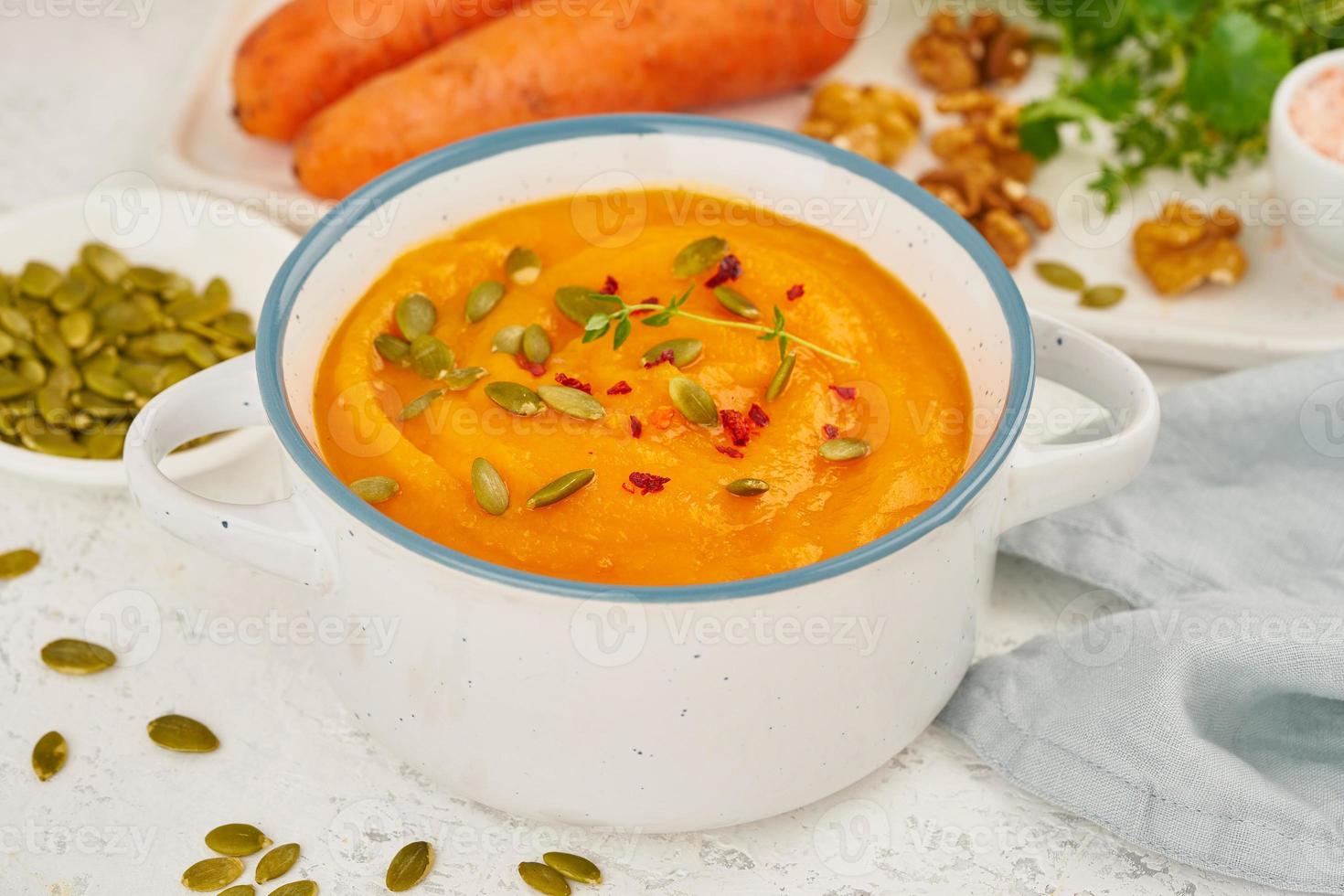 Carrot cream soup with pumpkin seeds and parsley and walnuts, side view on light background closeup photo