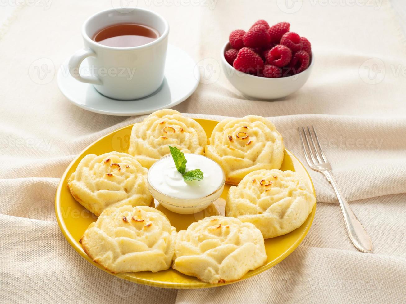 Diet cheese pancakes, rose shape, on yellow plate with tea, raspberry on textile linen napkin photo