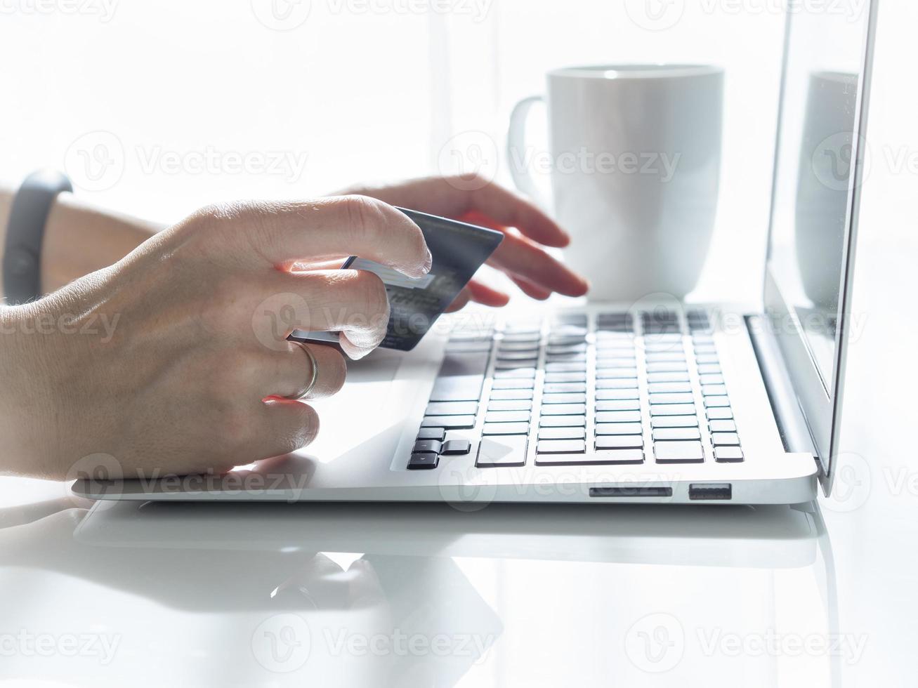 woman sitting at a table, drinking tea and looking at a laptop, pay for purchases photo