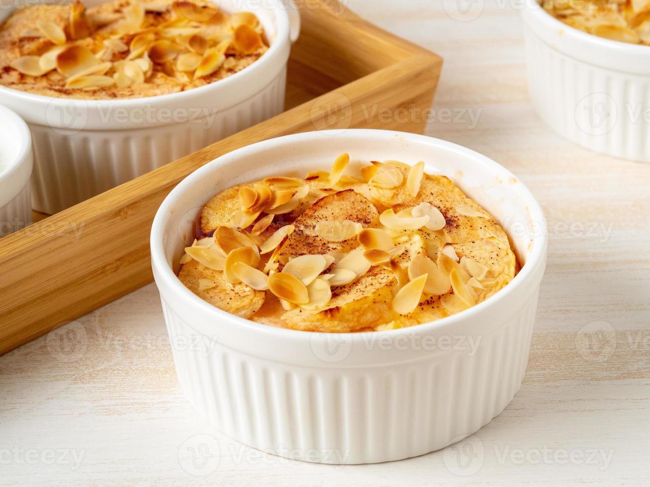 Cheesecake on white wooden table in kitchen. Delicate curd dessert with apples, almond flakes photo