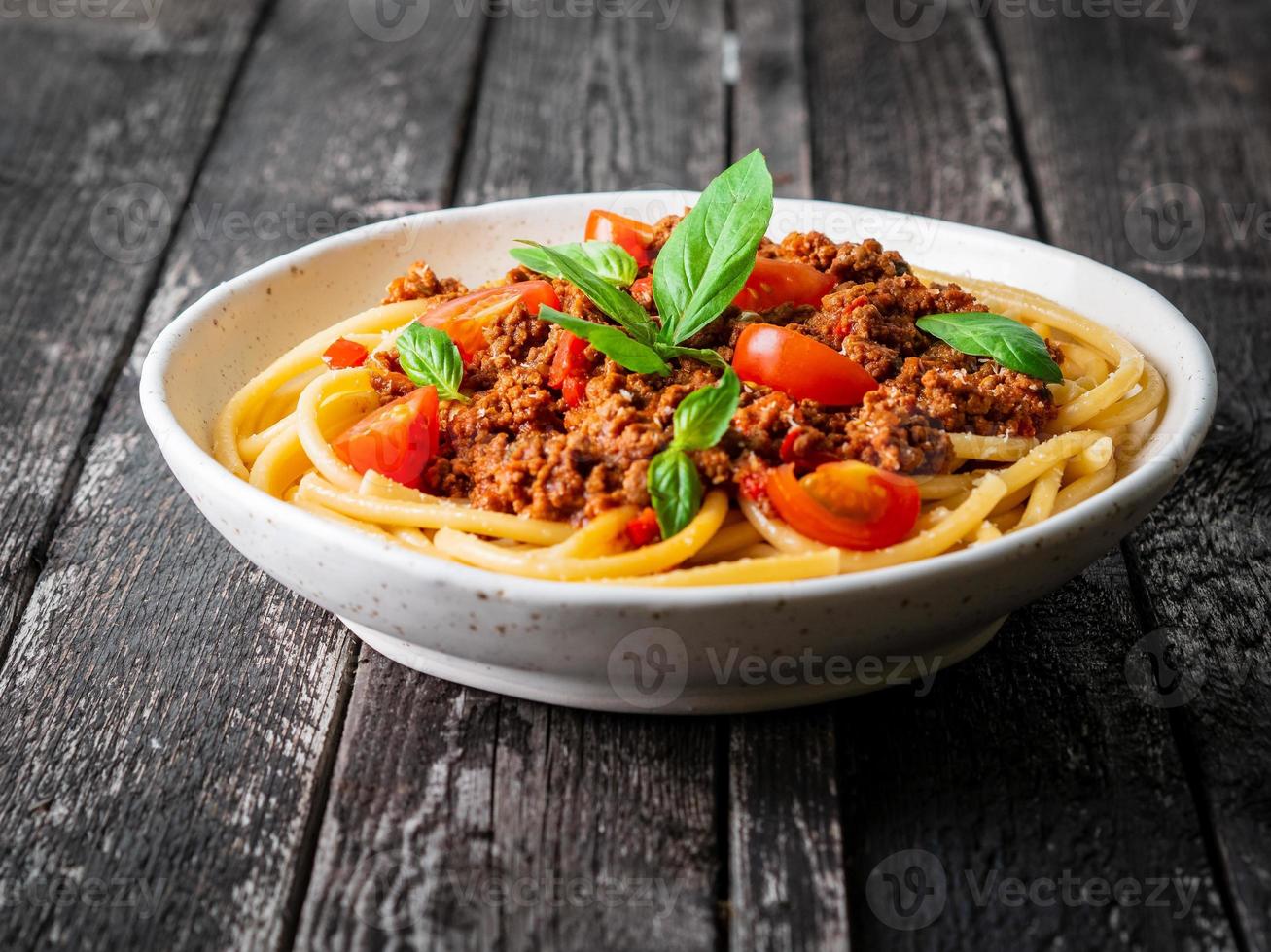 pasta bolognese with tomato sauce, ground minced beef, basil leaves on background photo