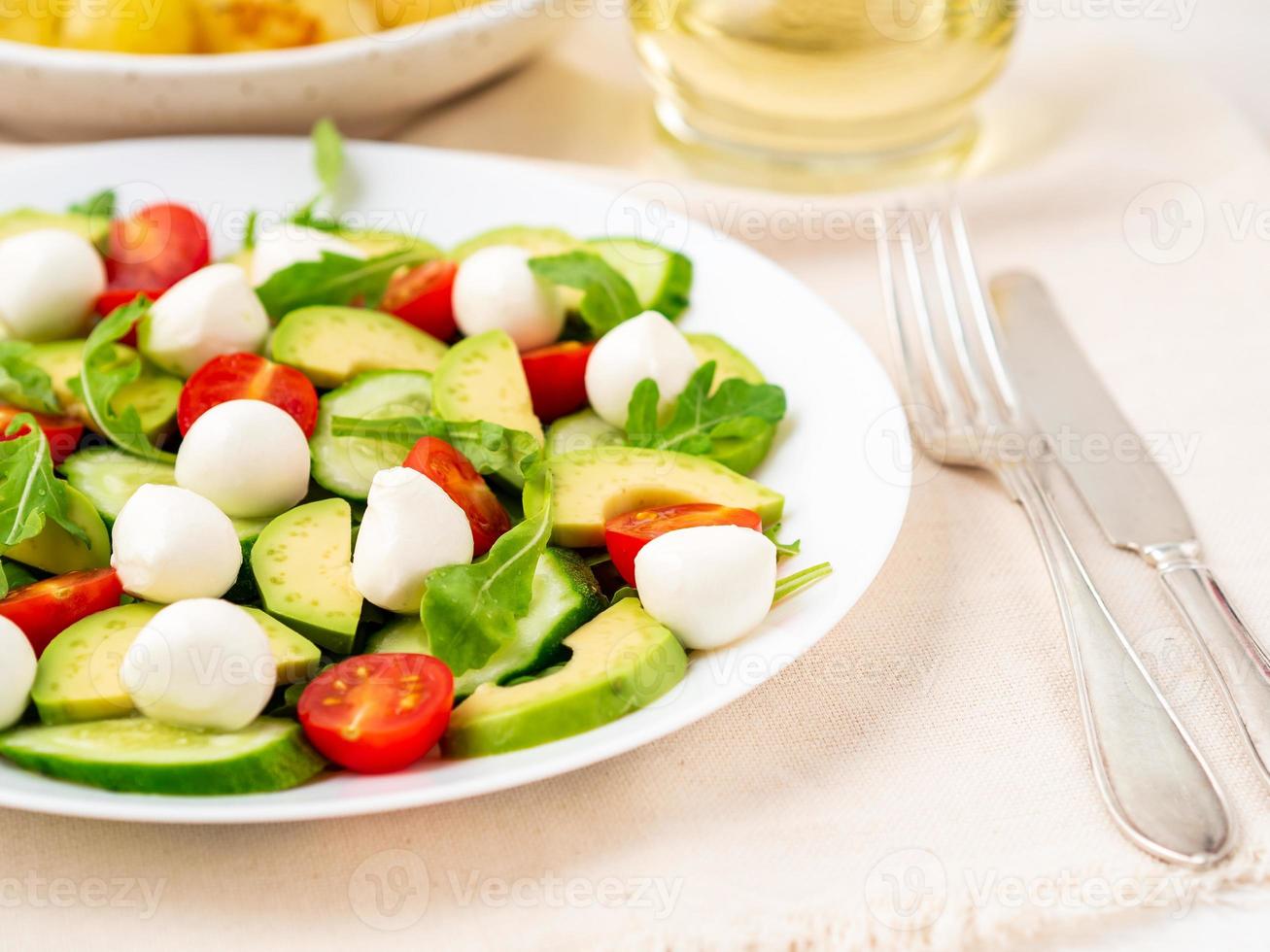 Fresh salad with tomatoes cucumbers arugula mozzarella and avocado. Oil with spices photo
