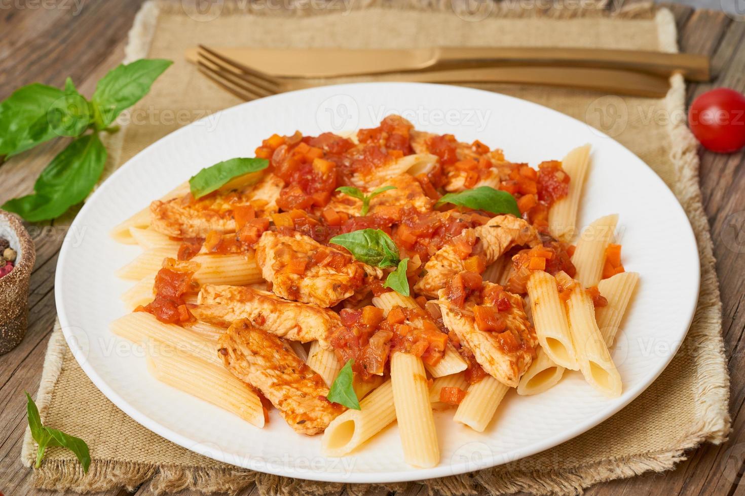 Penne pasta, chicken or turkey fillet, tomato sauce with a basil leaves on old rustic wooden background photo