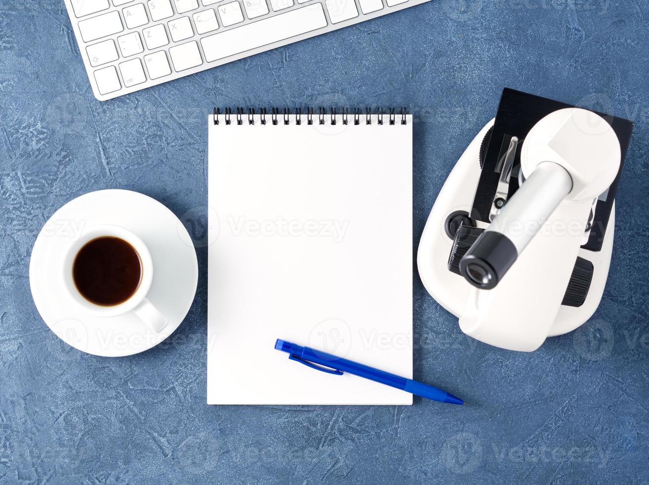 Top view of dark blue desktop with microscope, notepad, computer. Mock up, empty space, science photo