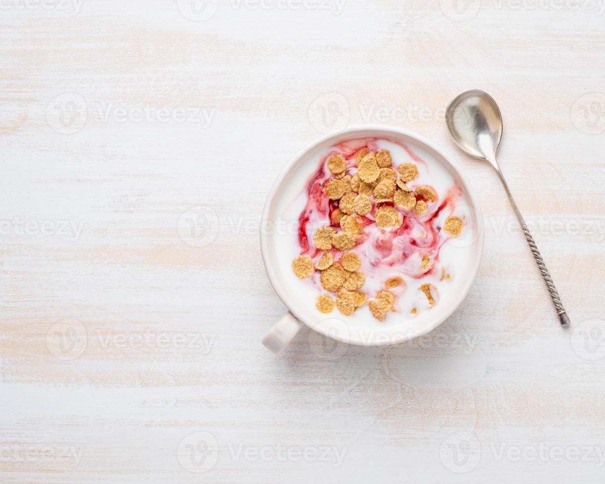 yogur griego con mermelada y muesli en tazón blanco sobre mesa de madera blanca, vista superior, espacio para copiar foto