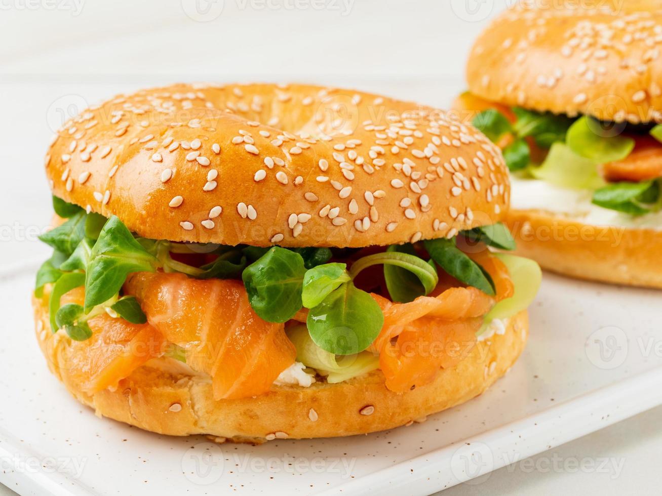 dos sándwiches con salmón, queso crema, rodajas de pepino sobre una mesa de mármol blanco foto