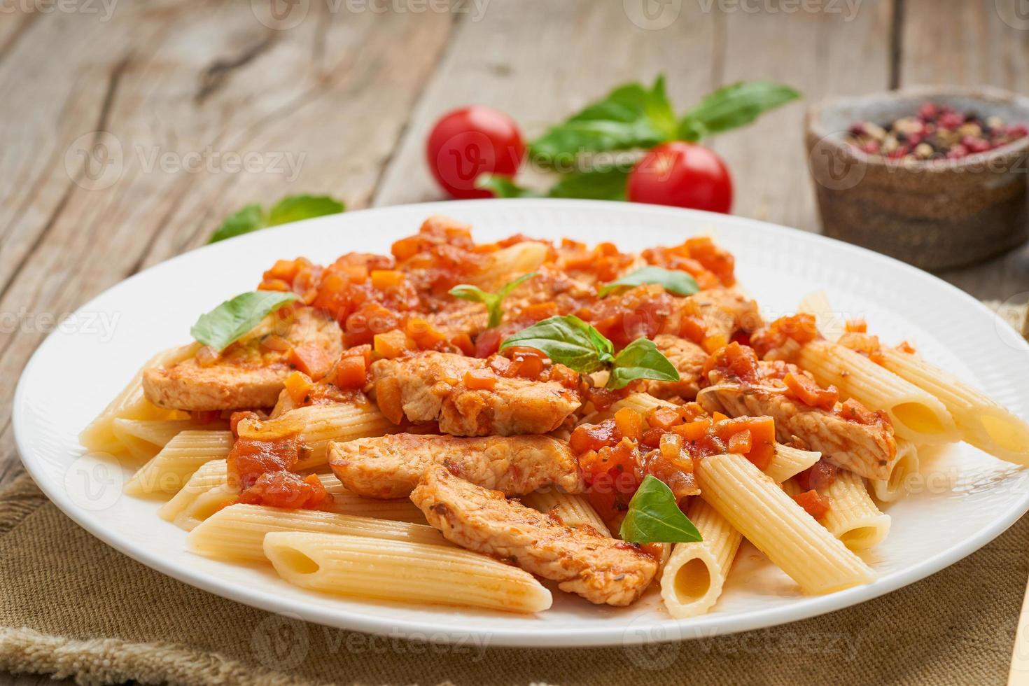 Penne pasta, chicken or turkey fillet, tomato sauce with basil leaves on old rustic wooden background. Close up, side view photo