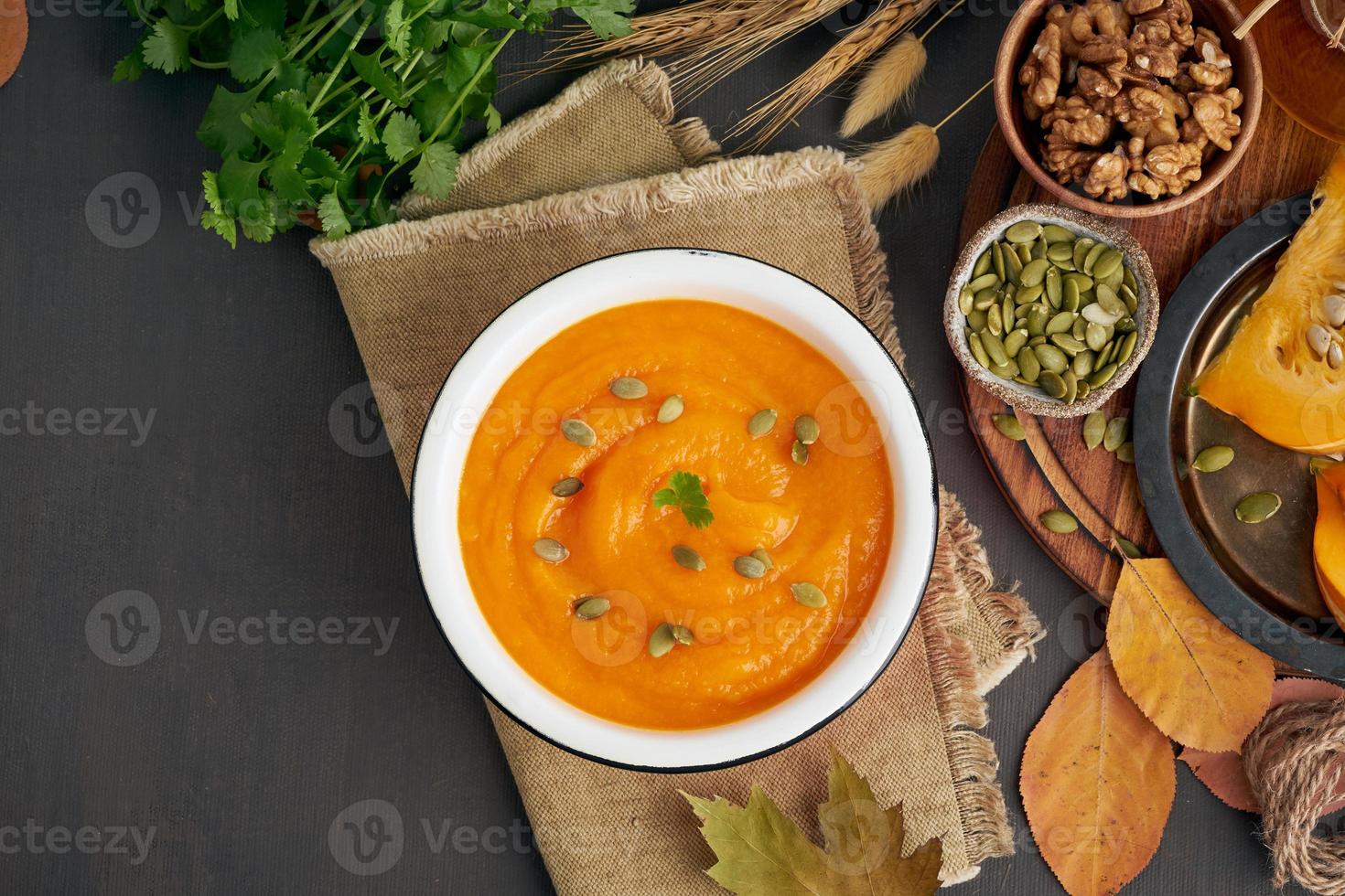 Pumpkin cream soup with walnut and seeds and parsley, dark wooden background photo