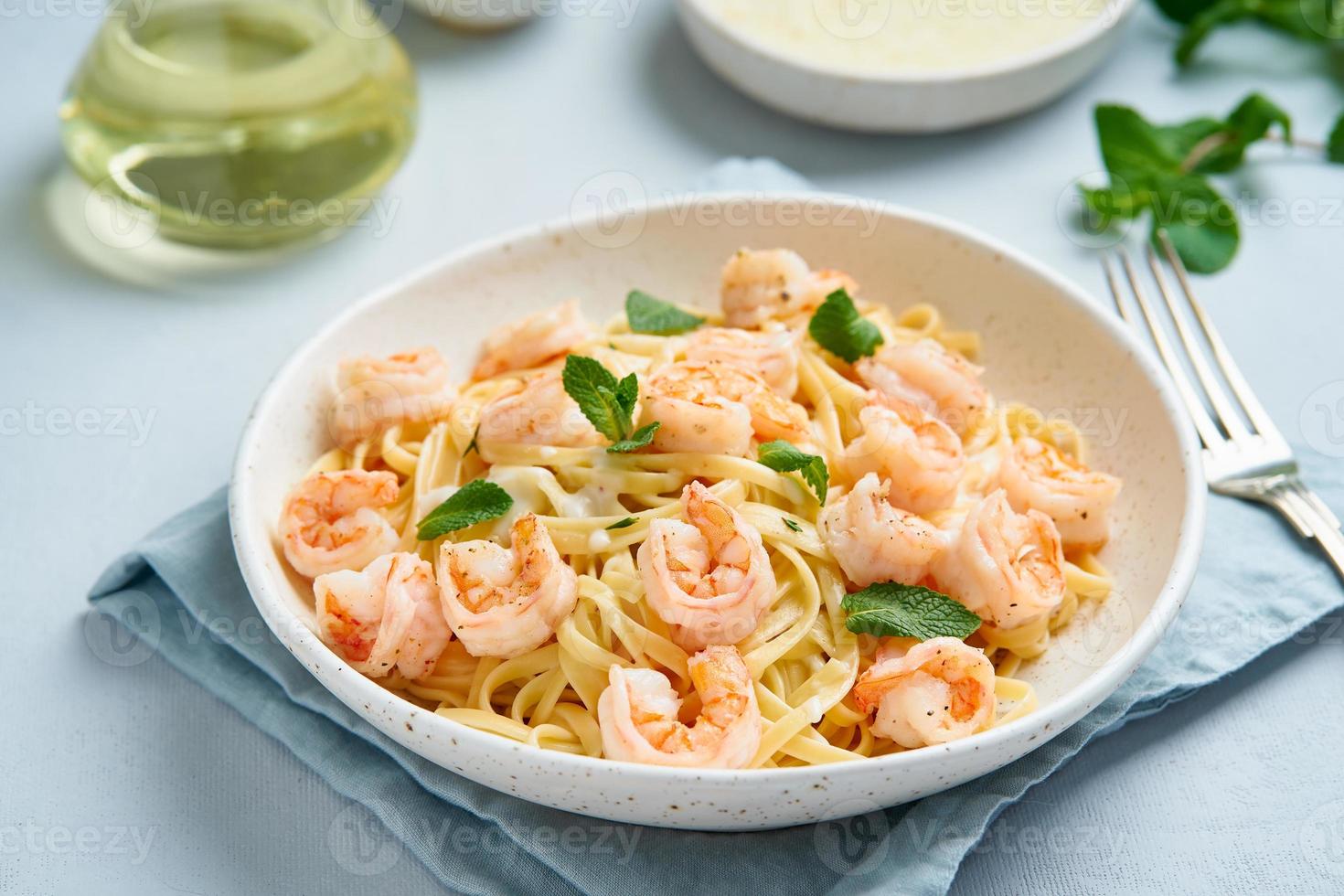 Pasta spaghetti with grilled shrimps, bechamel sauce, mint leaf on blue table photo