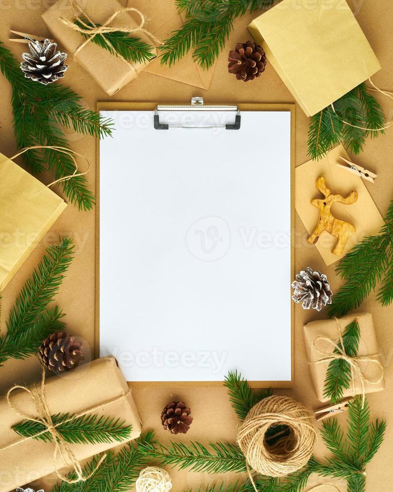 White open blank on clipboard and Christmas decoration lying on beige craft paper background, flat lay, copyspace. Hand crafted, plastic free, zero waste concept photo