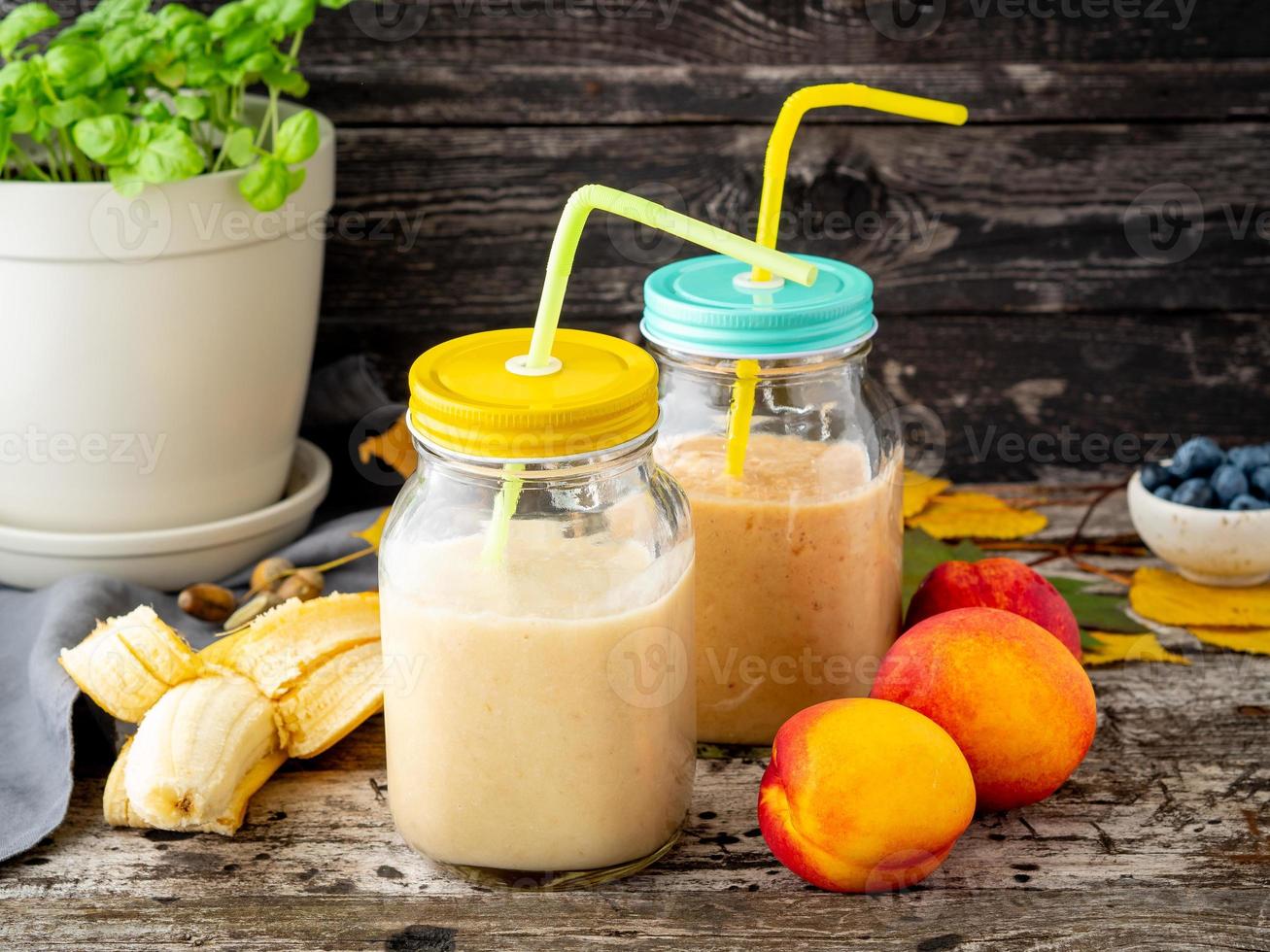 banana peach nectarine smoothie in two jars, fresh fruit milkshakes on old dark rustic wooden table, side view photo