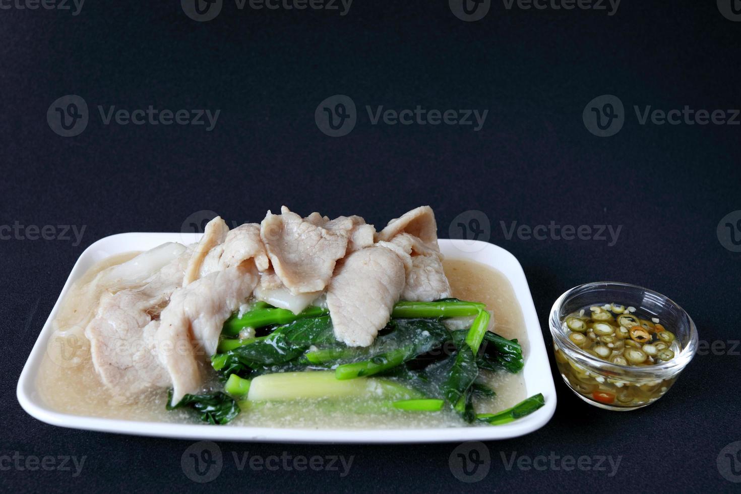 Fried noodle with pork in gravy sauce in white dish and glass bowl of slice green chilli in vinegar on black background, Chinese style in Thailand. photo