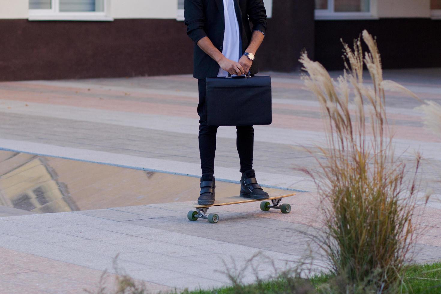 Concept of young,fast and mobile manager. Funny buisinessman on skateboard in black suit. photo