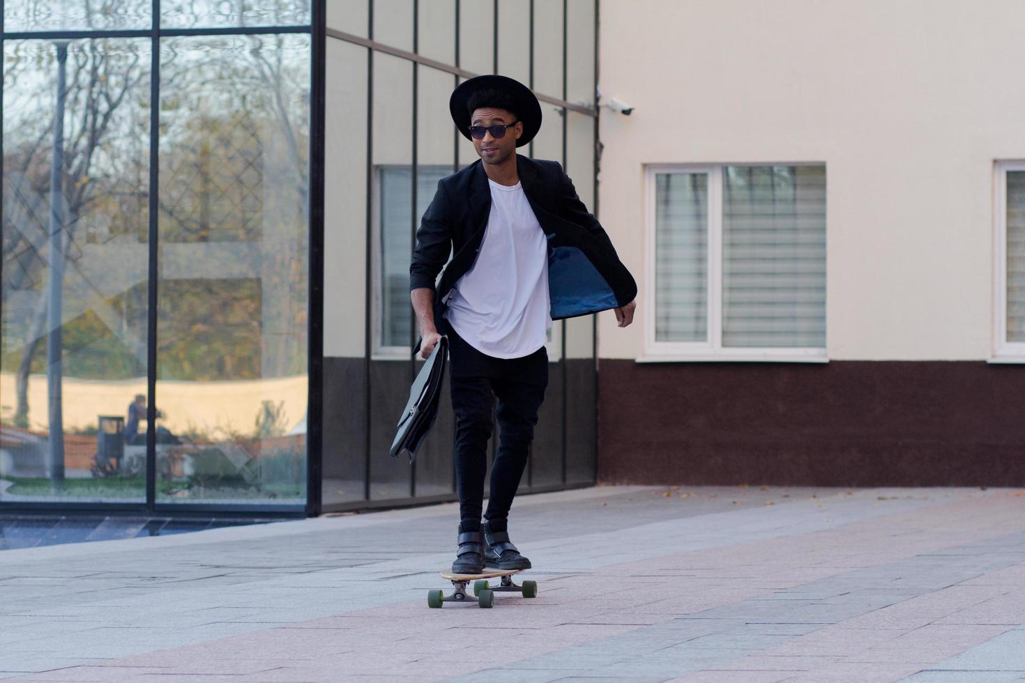 concepto de administrador joven, rápido y móvil. hombre de negocios divertido en patineta con traje negro. foto