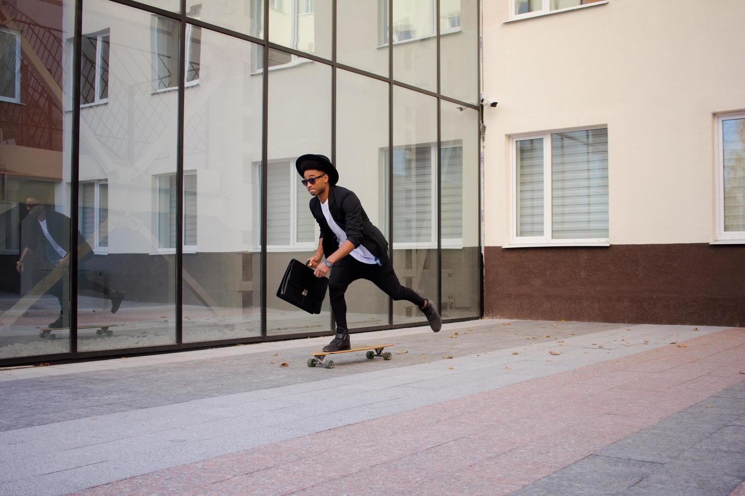 concepto de administrador joven, rápido y móvil. hombre de negocios divertido en patineta con traje negro. foto