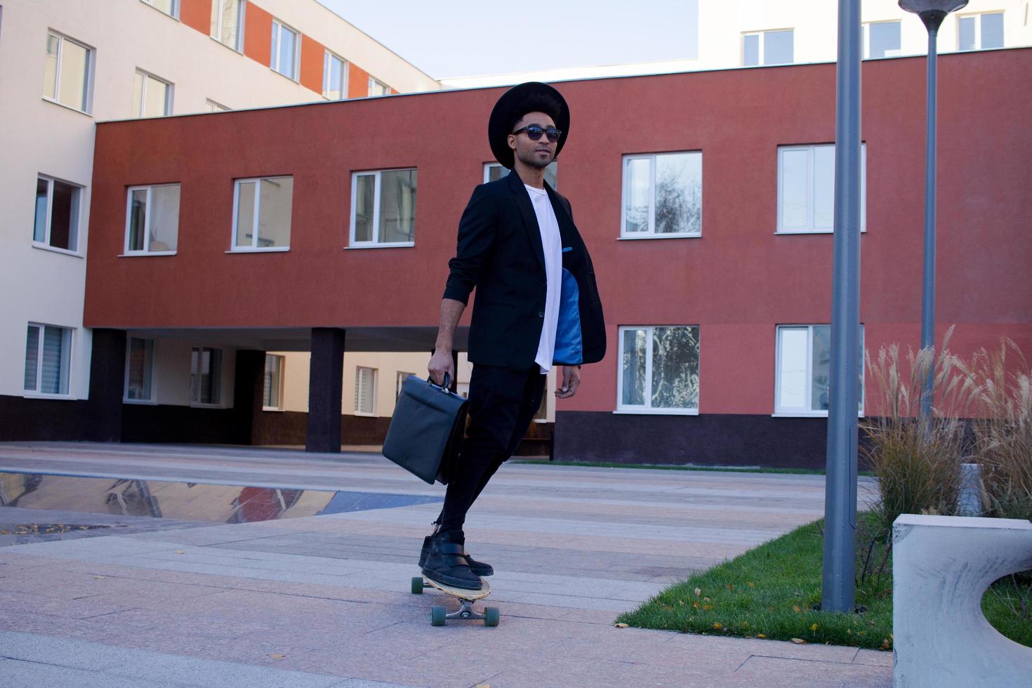 concepto de administrador joven, rápido y móvil. hombre de negocios divertido en patineta con traje negro. foto