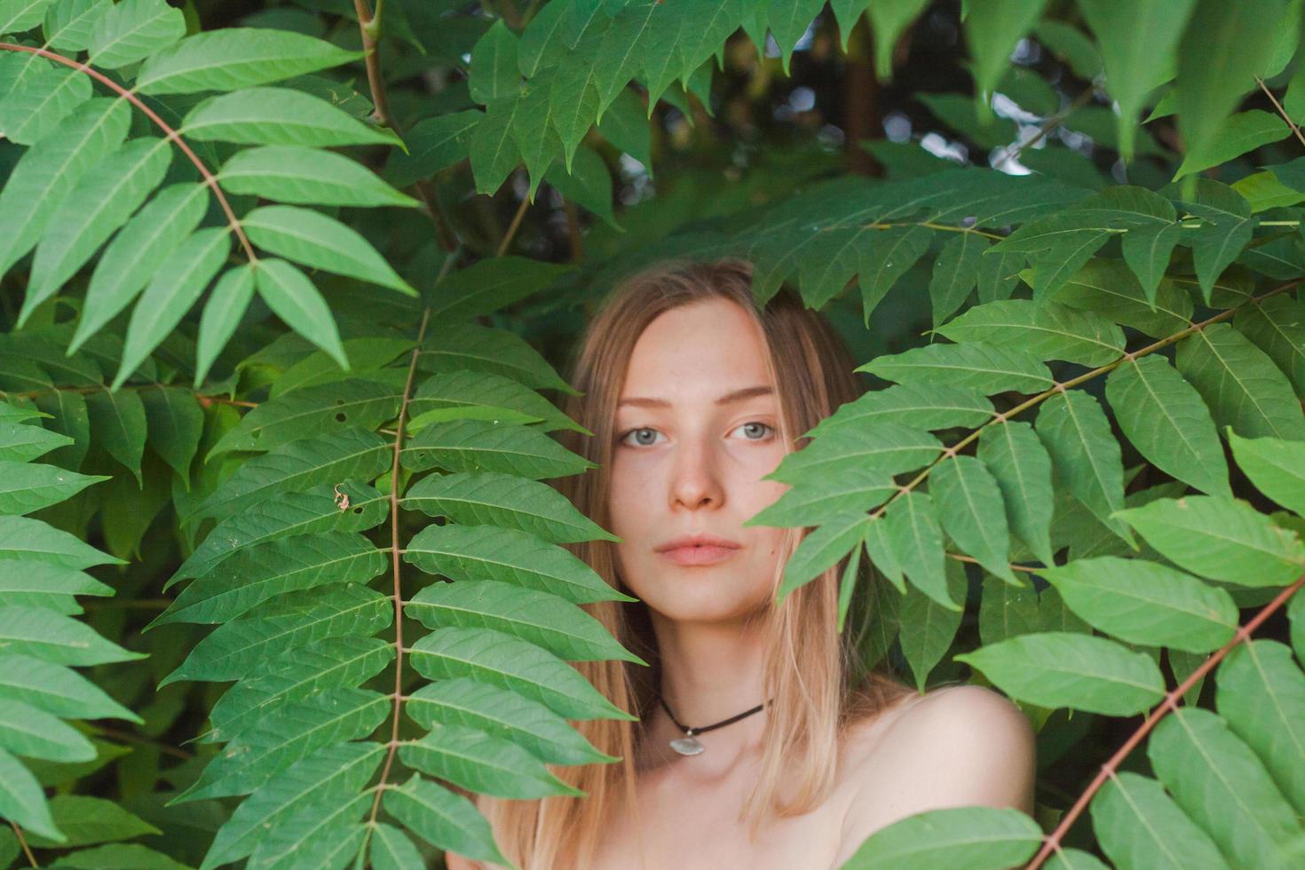 retrato de una bella joven con hojas verdes, una bella dama rubia con arbustos de primavera foto