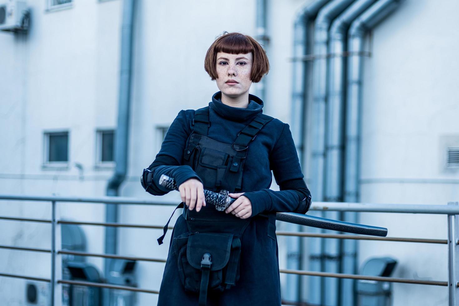 portrait of young redhead woman with japanese sword dressed in futuristic cyberpunk costume standing on the roof. photo