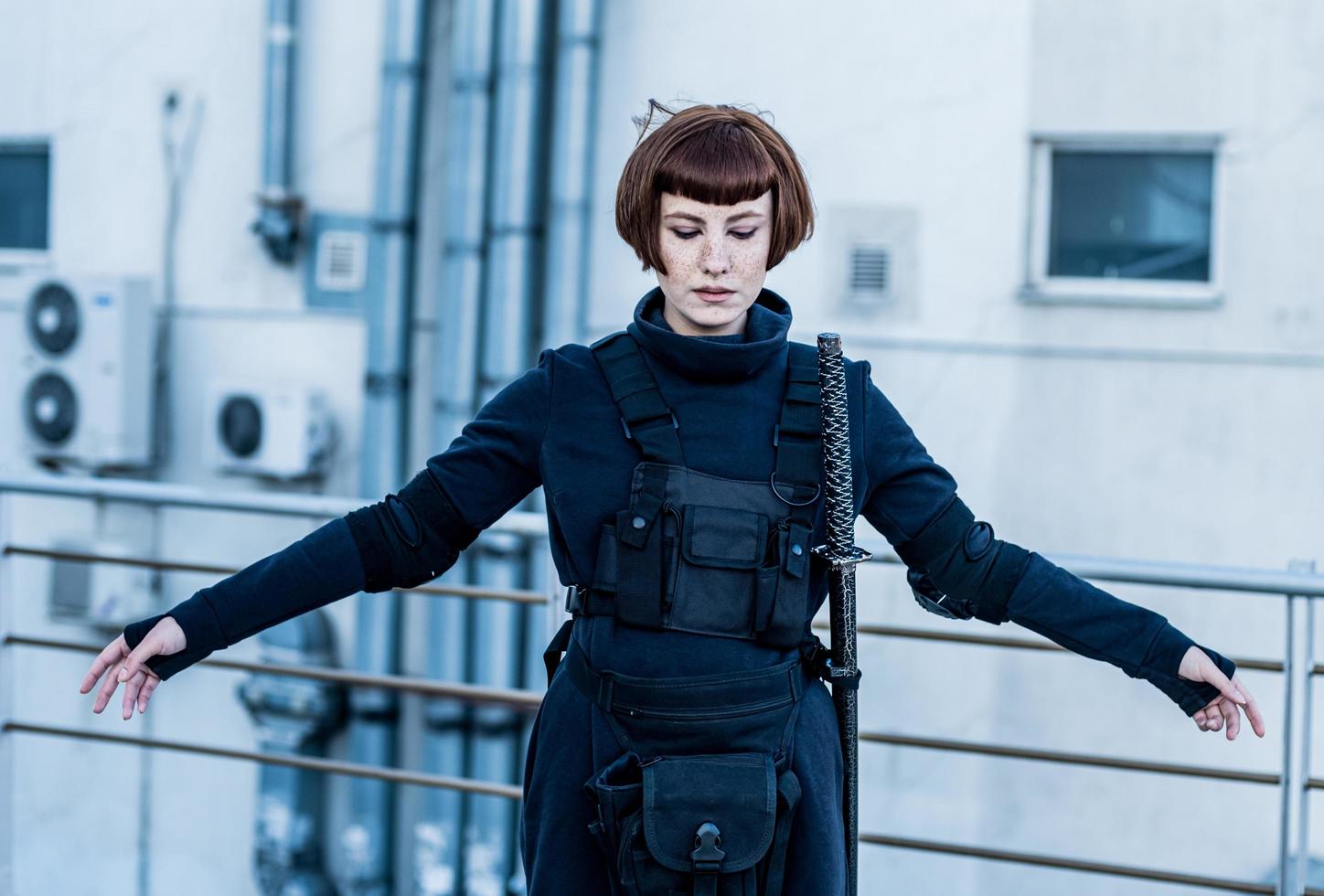 portrait of young redhead woman with japanese sword dressed in futuristic cyberpunk costume standing on the roof. photo