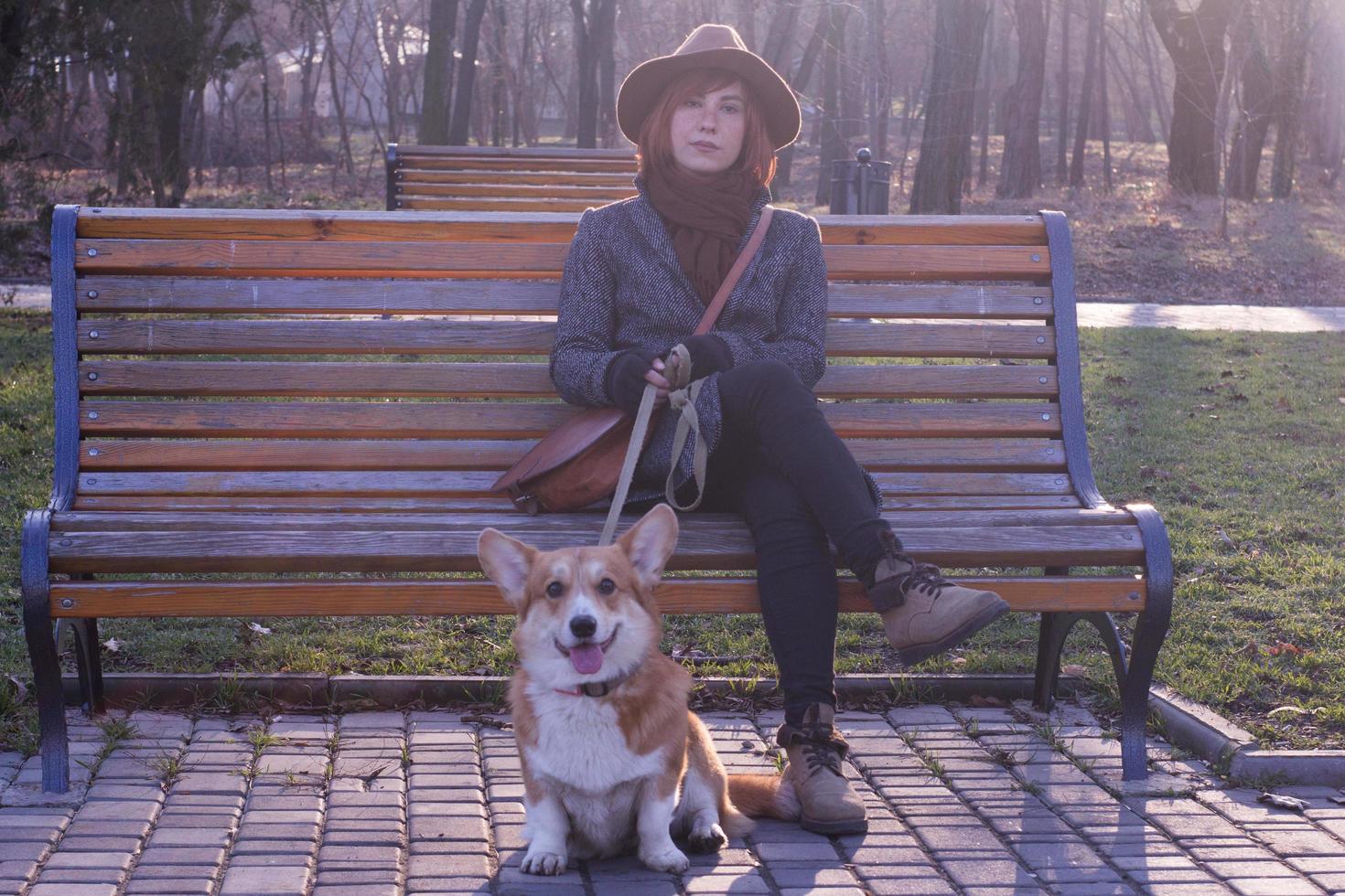 mujer joven con sombrero en el paseo por el parque con un lindo perro corgi, un día soleado de otoño foto