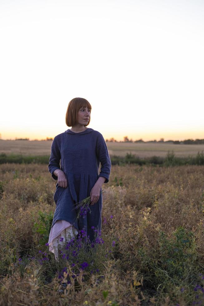 Young redhead woman with freckles in vintage handmade dress walk in fields with flowers photo