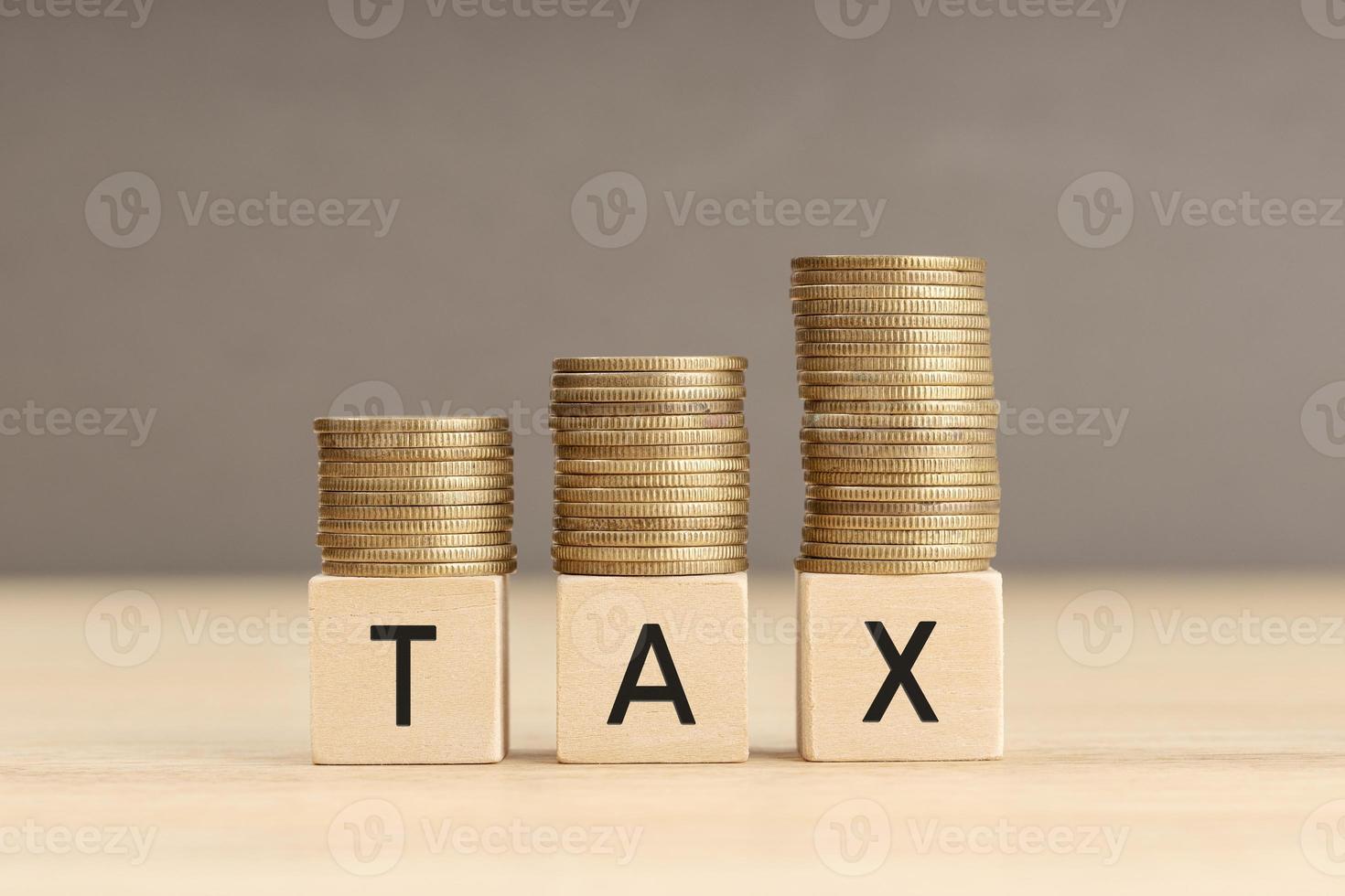 Tax word in wooden blocks with coins stacked in increasing stacks. Tax increasing concept. Copy space photo