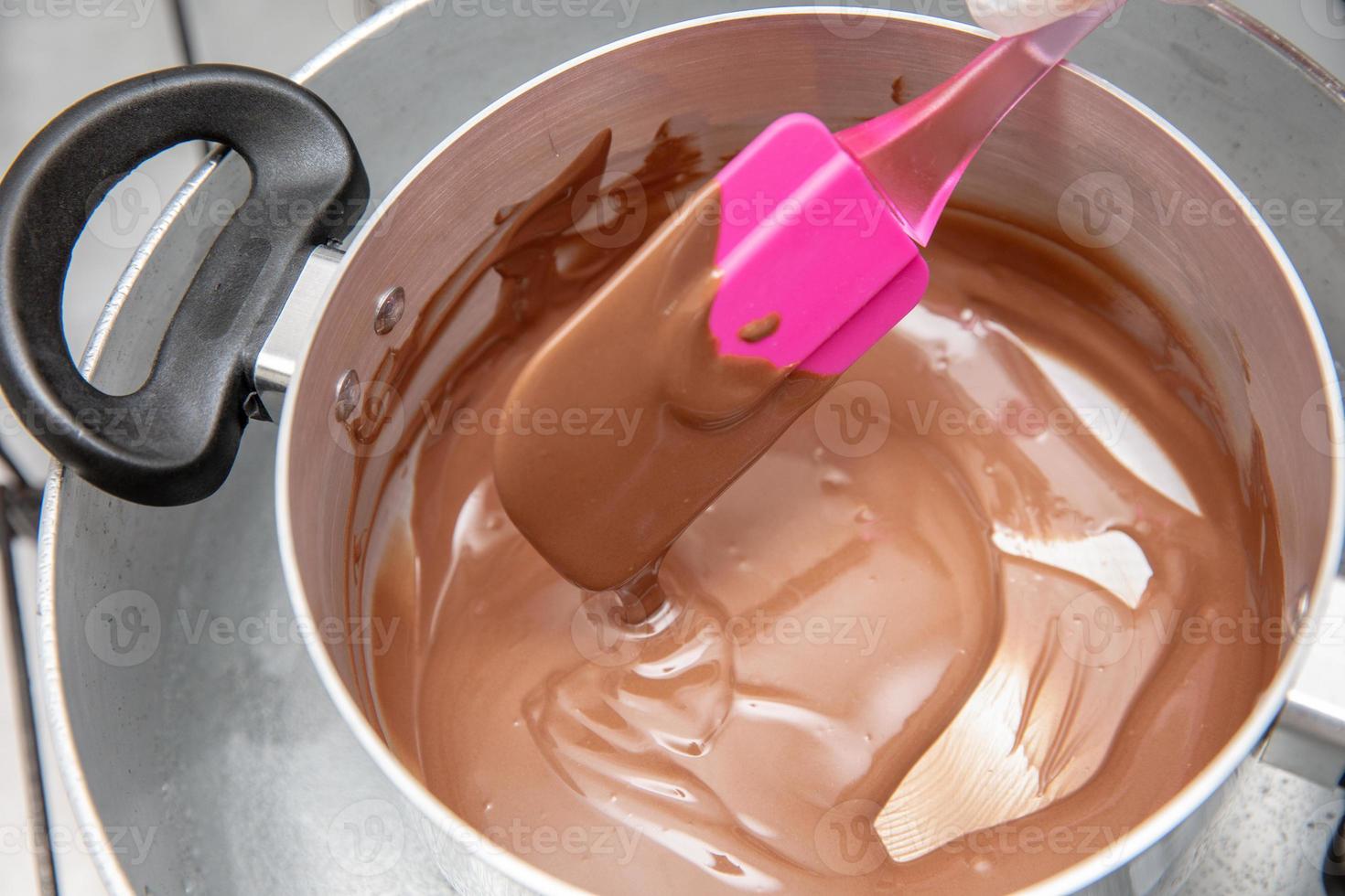 Cooking pot with chocolate melting being removed by chef hand on the stove of a kitchen to make sweet desserts. Bulk chocolate melting in a pot. photo