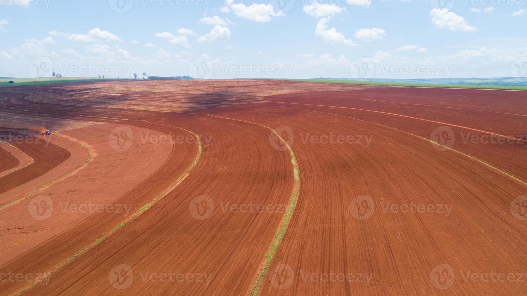 Aerial view of tractor with mounted seeder performing direct seeding of crops on plowed agricultural field. Farmer is using farming machinery for planting process, Brazilian farm. photo