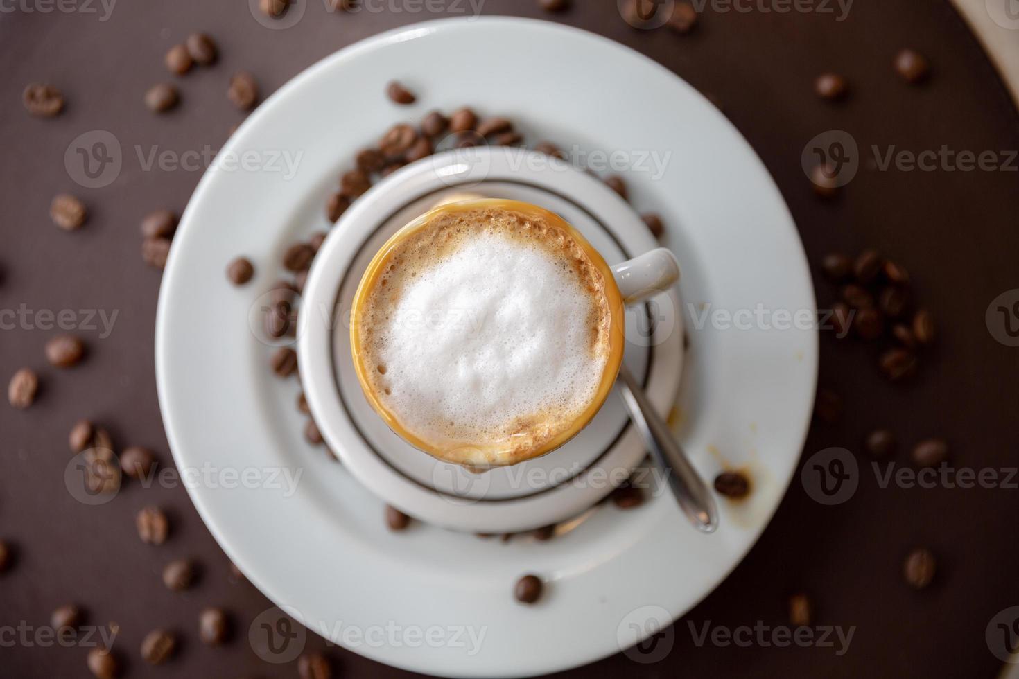 Cappuccino with nice frothy foam. Latte art with a heart made from milk. Coffee cup with a saucer and a teaspoon on a table. photo
