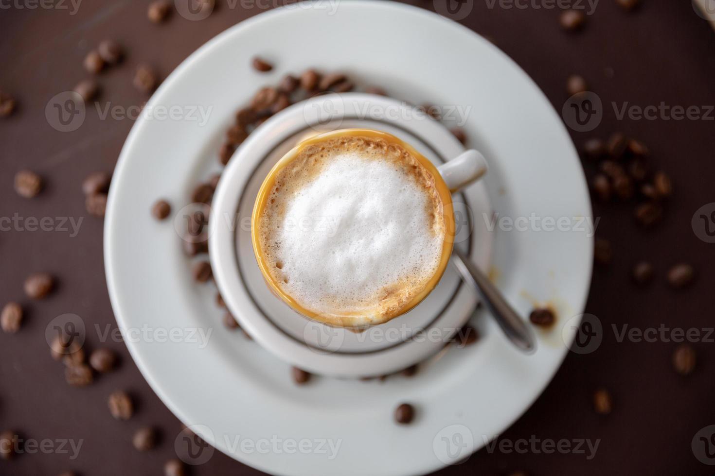 Cappuccino with nice frothy foam. Latte art with a heart made from milk. Coffee cup with a saucer and a teaspoon on a table. photo