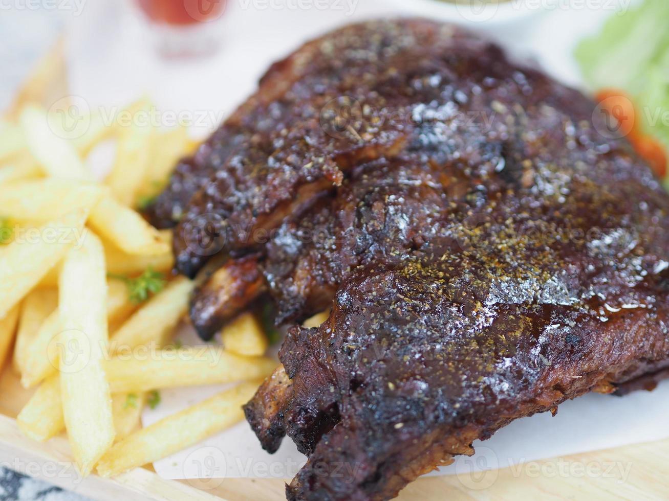 Pork Spareribs BBQ, Barbeque Pork Ribs with french fries vegetable salad, tomato sauce in a clear glass on wooden tray, food photo