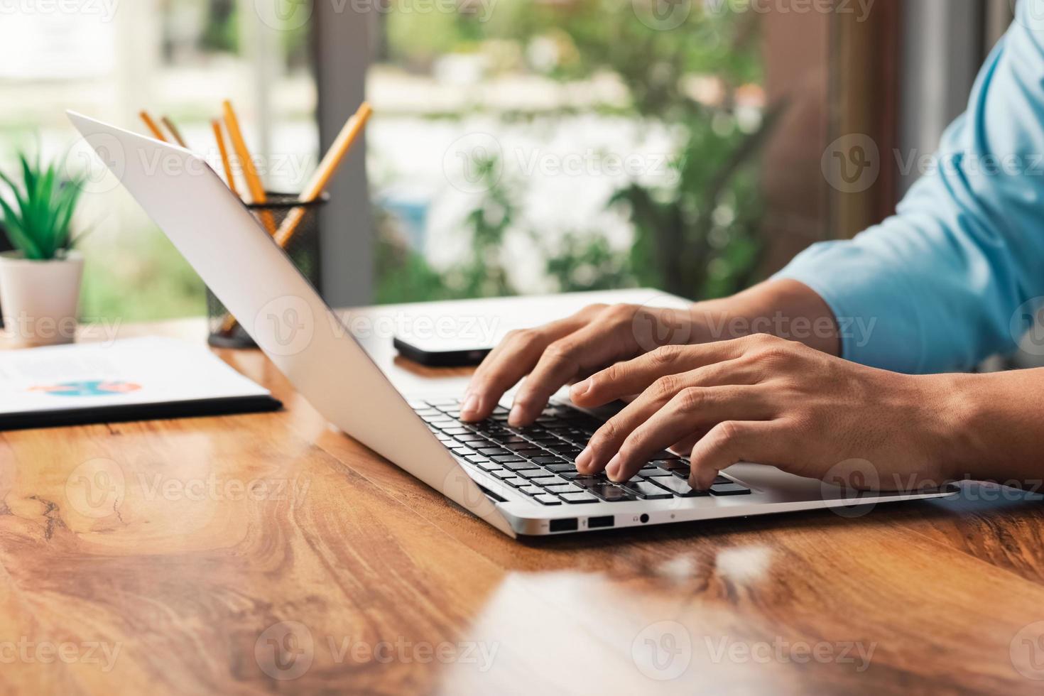 young man using laptop computer and mobile phone When looking for financial information in business, work at the desk. Writing with a pen, studying remotely from home and working from home. photo