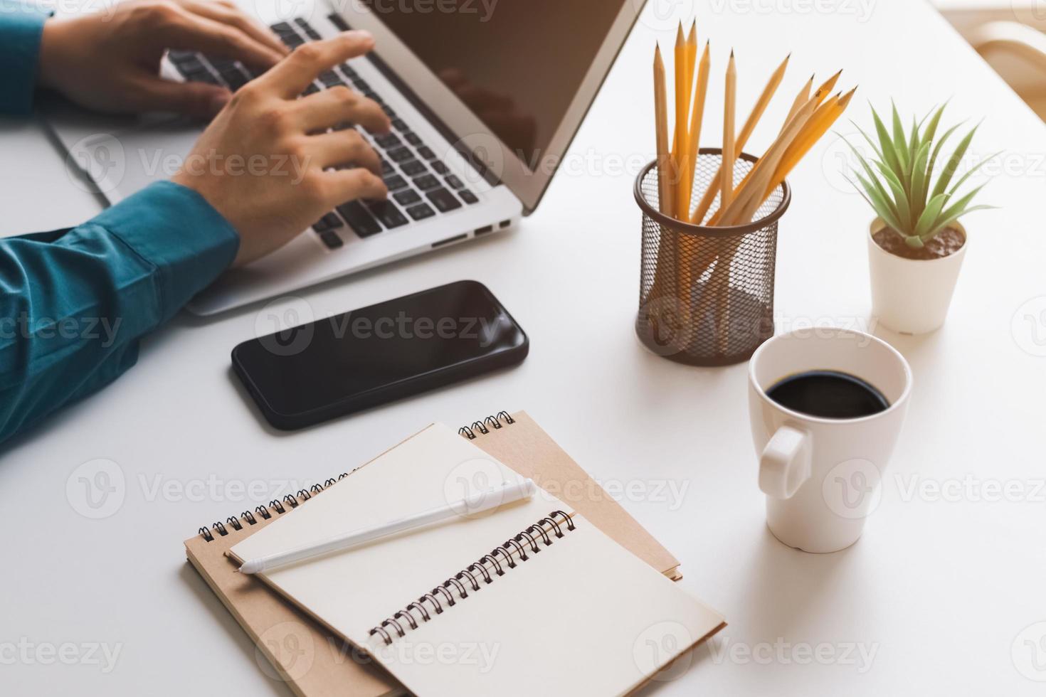 young man using laptop computer and mobile phone When looking for financial information in business, work at the desk. Writing with a pen, studying remotely from home and working from home. photo