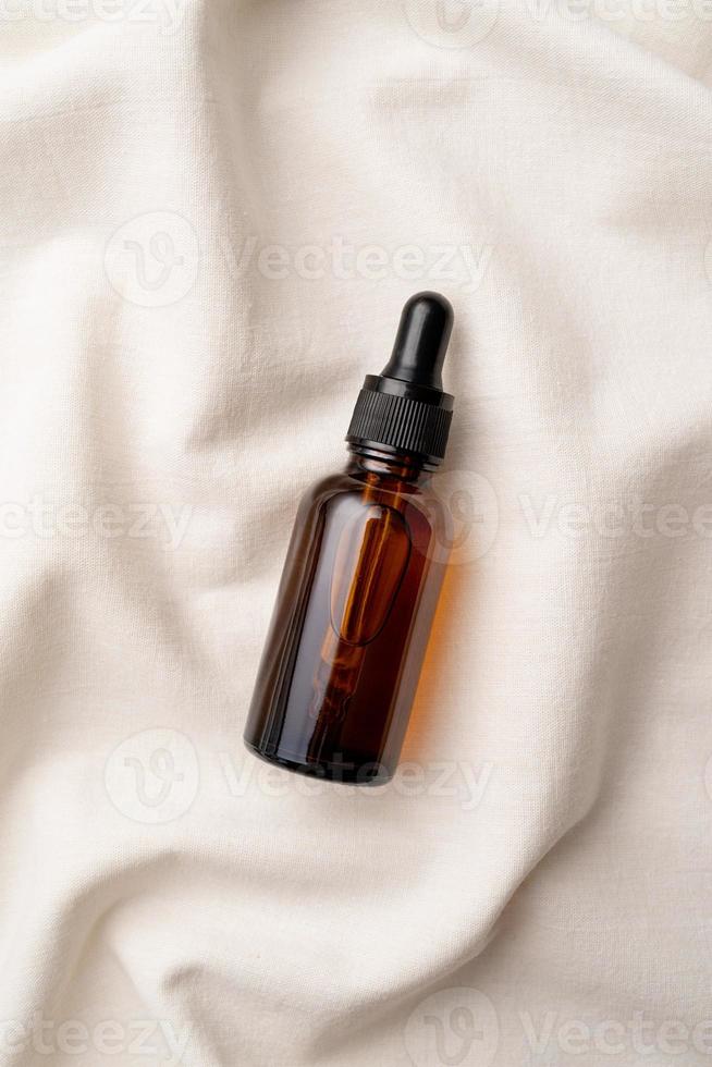 top view of amber glass essential oil droppper bottle with pipette on fabric wavy background photo