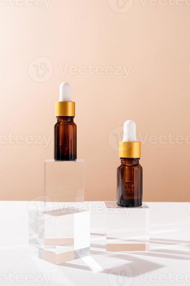 Amber glass dropper bottles with a pippette with white rubber tip on glass podium and beige background, mockup design photo