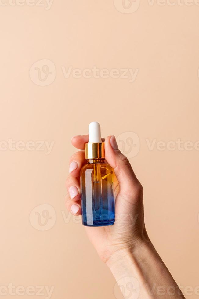 Dropper Bottle Mock-Up. Female hand holding amber glass dropper bottle on beige background photo