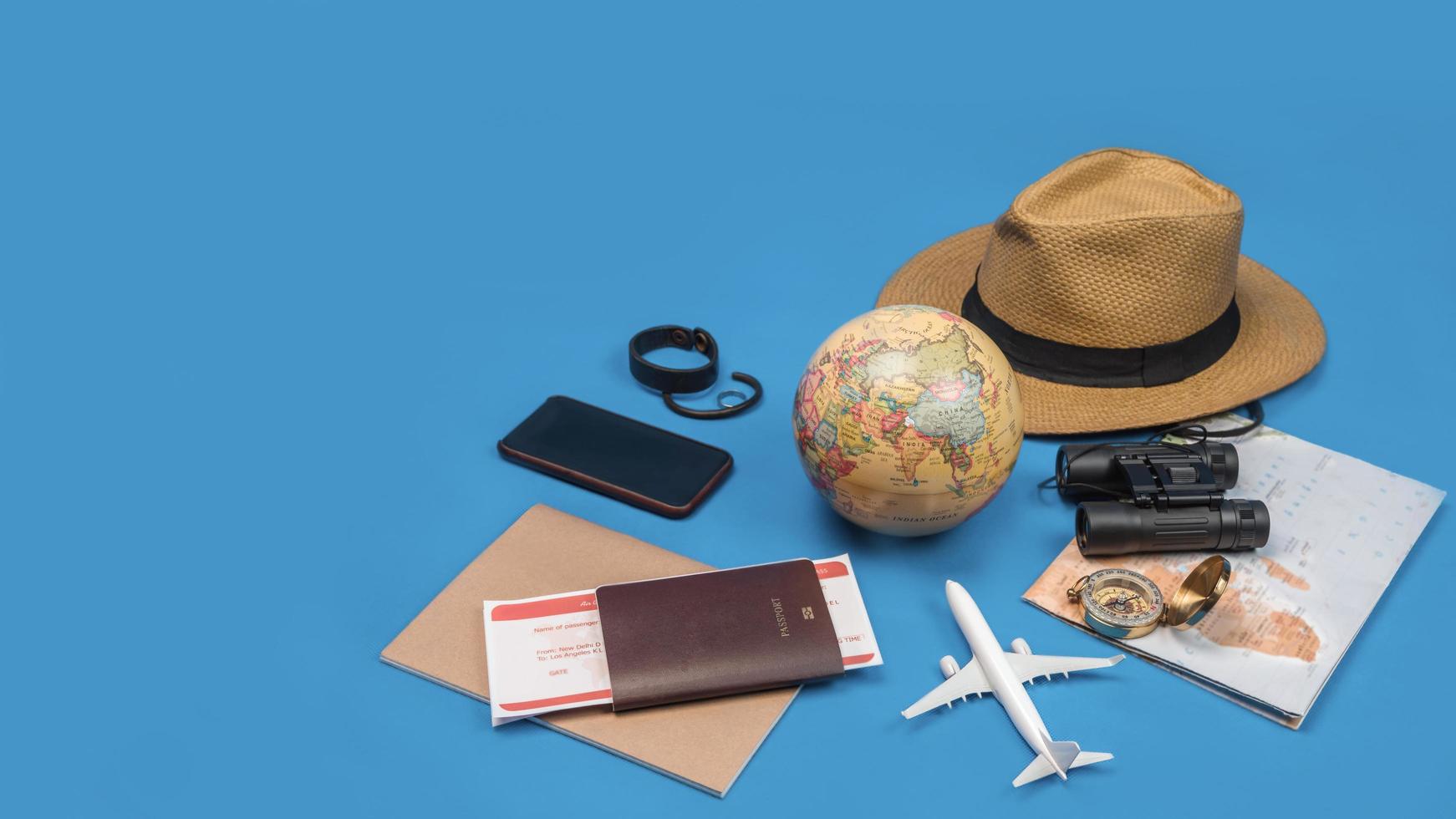 vacaciones de planificación turística con la ayuda del mapa del mundo con otros accesorios de viaje alrededor. teléfono inteligente, cámara de película y gafas de sol sobre un fondo azul. foto