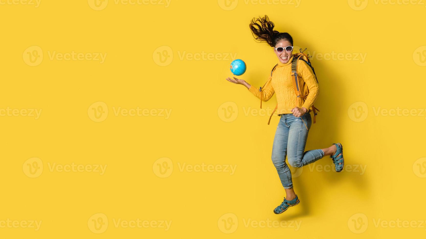 mujer viajera con maleta, sosteniendo globo terráqueo en la mano sobre fondo amarillo. retrato de niña feliz sonriente con espacio copia el texto. mochila de viaje foto