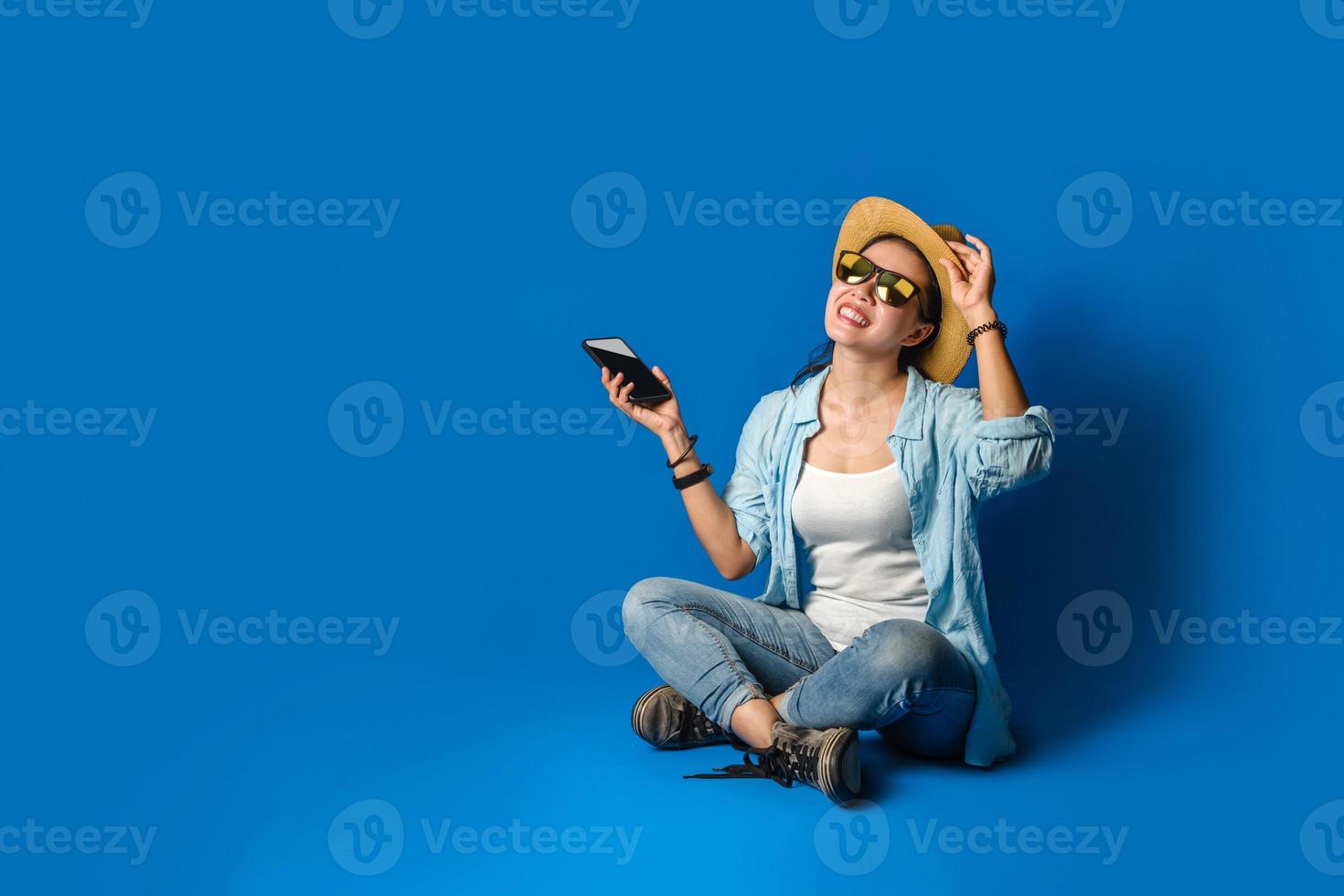 una hermosa niña con un vestido azul está sonriendo feliz con una cara alegre y sosteniendo teléfonos móviles en la mano, sobre fondo de color azul. mujer viajera foto