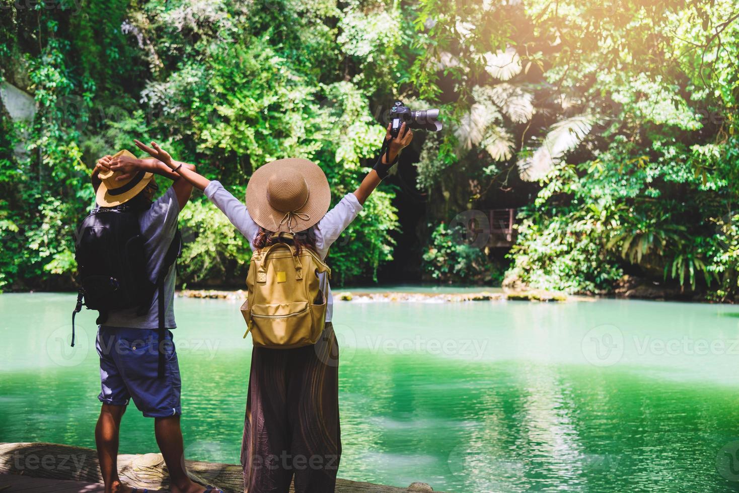 Couple travelers with backpacks relaxing in greens jungle and enjoying view in waterfall. stylish hipster traveler walking in sunny tropical forest. Tourism, hiking nature study. Couples traveling photo