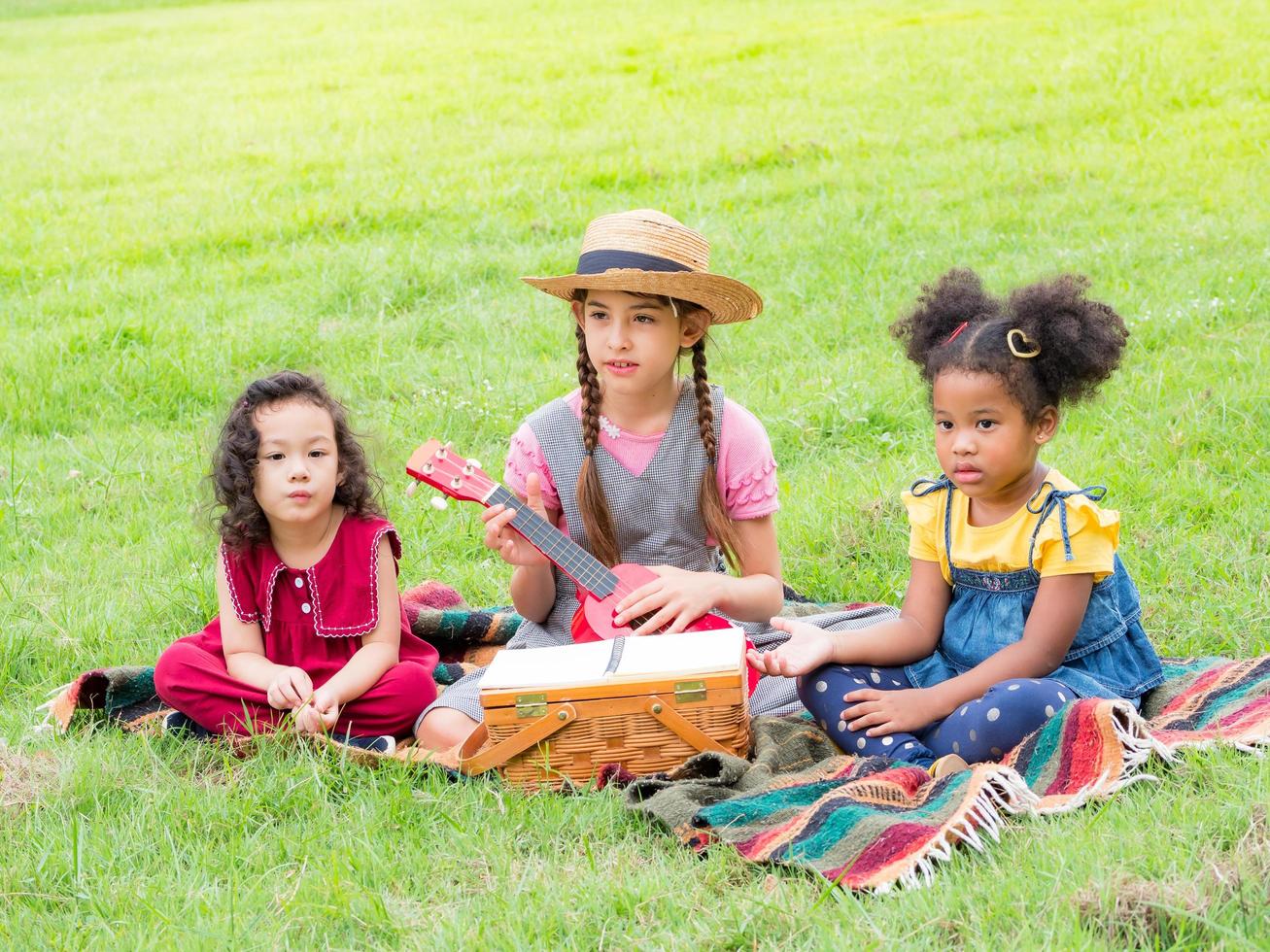 la niña se sienta en el césped y aprende a tocar el ukelele, aprendiendo fuera de la escuela en el parque natural foto