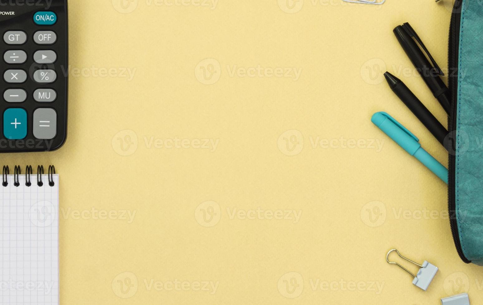 Top view of a Desk with a pencil case, pens, Notepad and calculator on a yellow background. Creative concept with back to school. Flat lay of items with space for text. photo